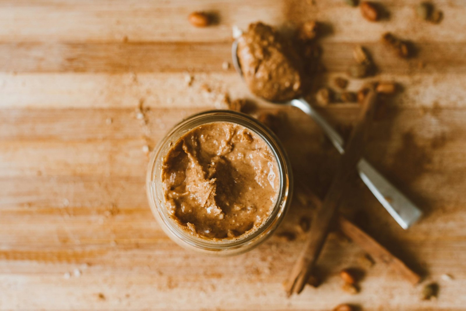 Creamy peanut butter in a jar with spoon on wooden surface, offering a rustic kitchen vibe.