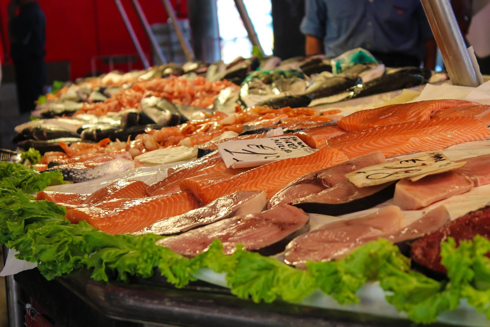 A variety of fresh seafood on display at a market stand with leafy greens, perfect for culinary inspiration.