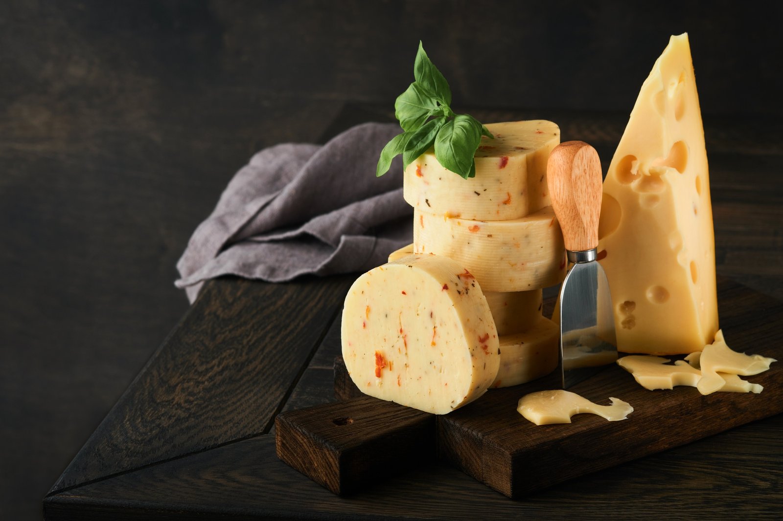 Stack of cheese with tomatoes and seasoning and Swiss cheese on with basil and knife on serving boar